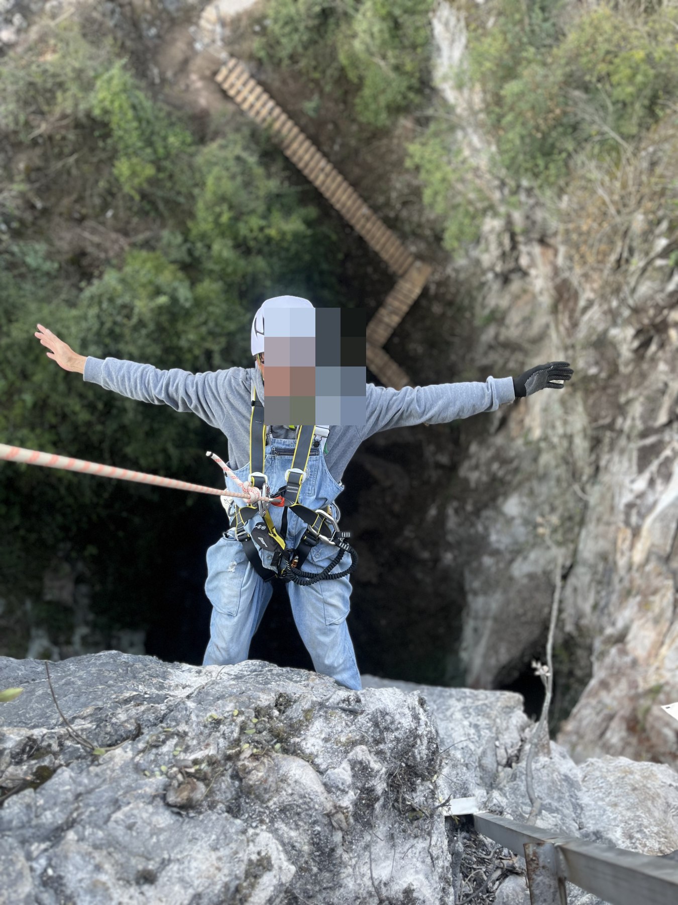 A helmeted and harnessed participant beside a rock opening